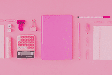 Elementos de papelería como libreta, folios, calculadora, bolígrafos, etc, de color rosa sobre un fondo rosa