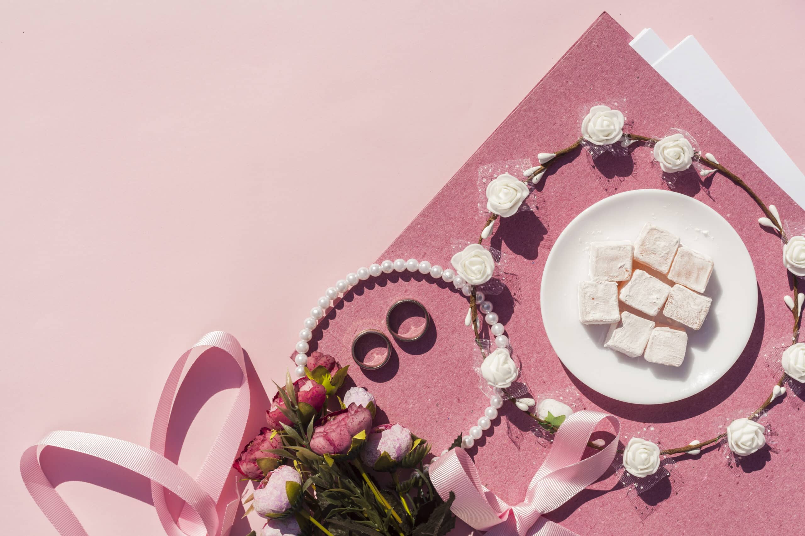 Elementos de bisutería sobre unsos folios rosas con decoraciones rosas sobre un fondo rosa